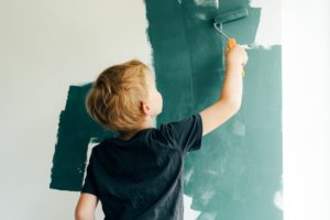 A boy paints a wall in a room by the window. Updates in the apartment. Repair yourself.
