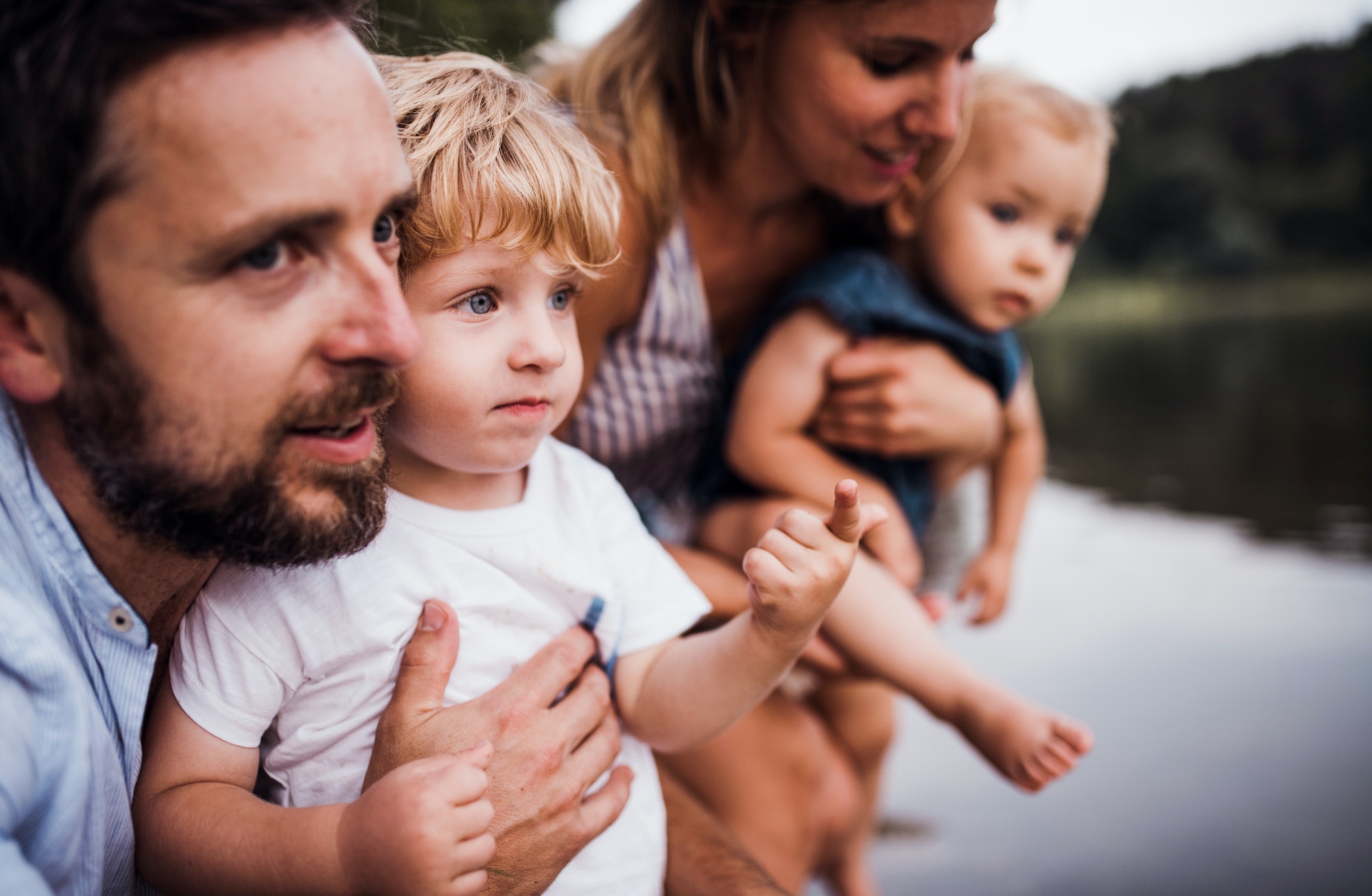 A young family with two toddler children outdoors by the river in summer.