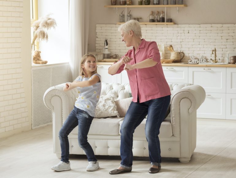 Cheerful older lady with her granddaughter dancing at home