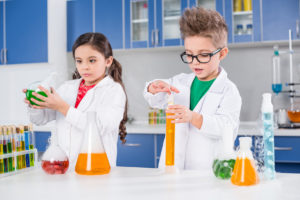 Concentrated little kids in lab coats making experiment in chemi