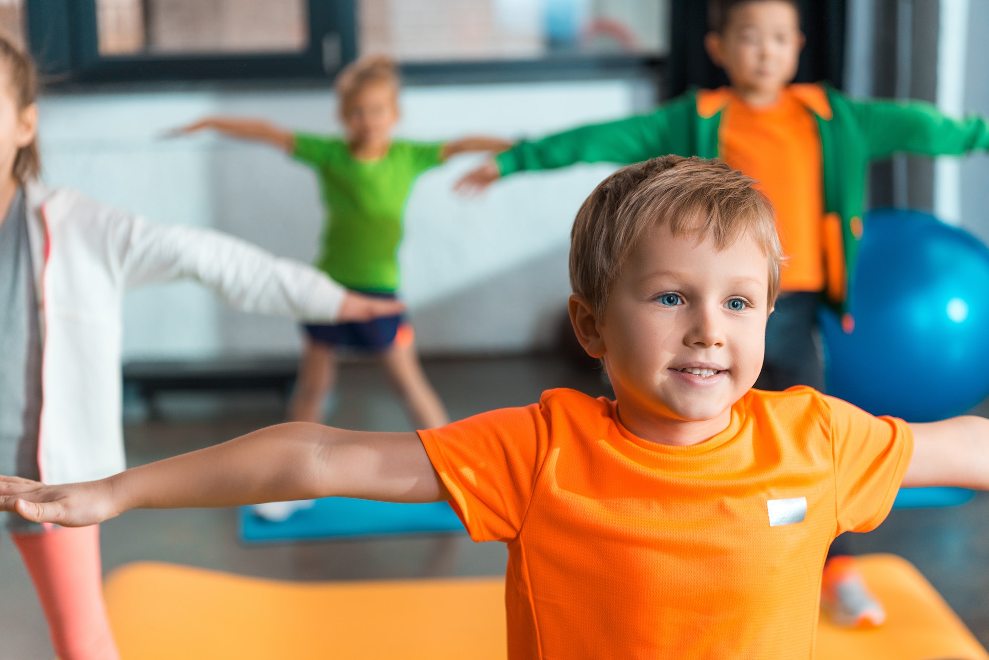Selective focus of multiethnic kids doing exercise with outstretched hands in sports center