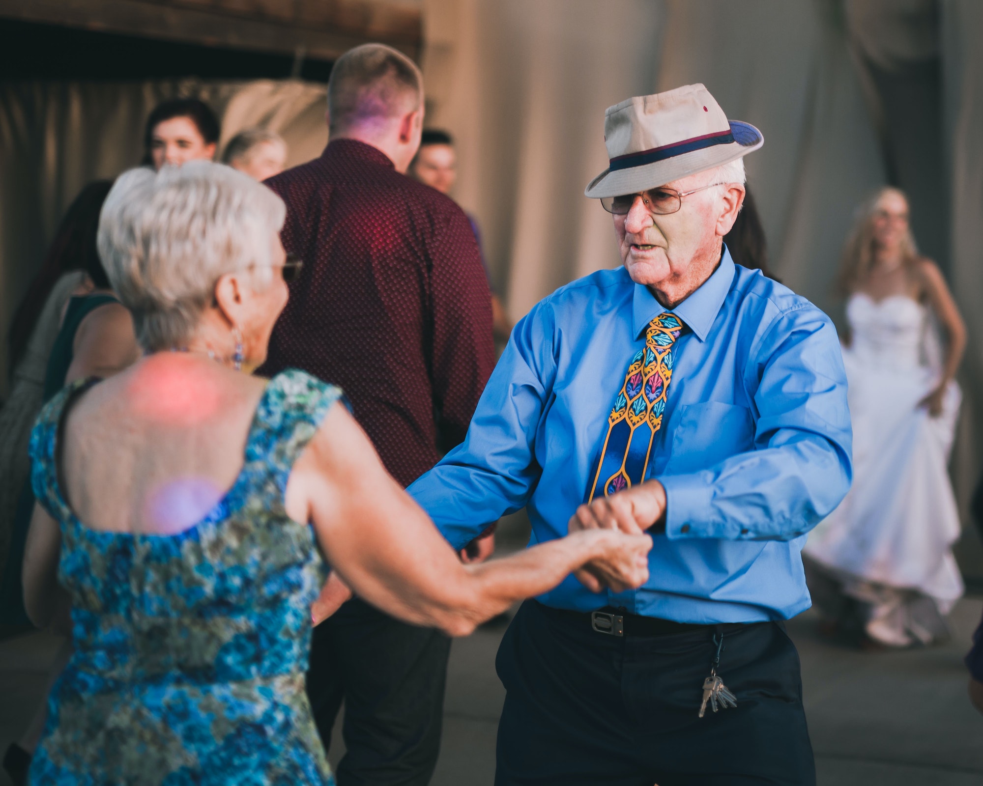 Two active seniors dance on the dance floor at a wedding during sunset.