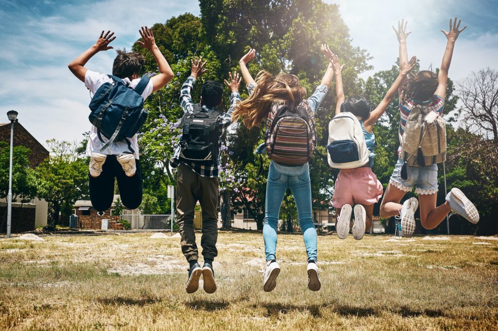 Schools out. Rearview shot of a group of unidentifiable schoolchildren jumping in the park.